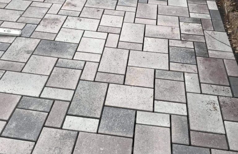 Gepflasterte Fläche mit grauen und beigen Steinplatten in unterschiedlichen Formen.