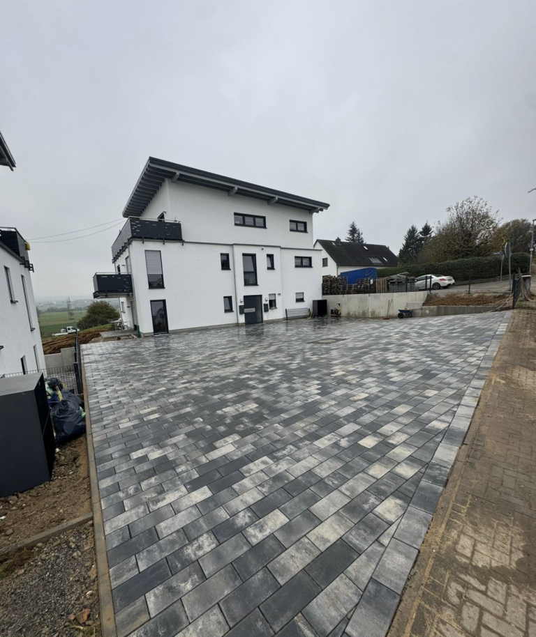 Moderne, zweigeschossige Architektur mit gepflastertem Vorplatz und bewölktem Himmel.