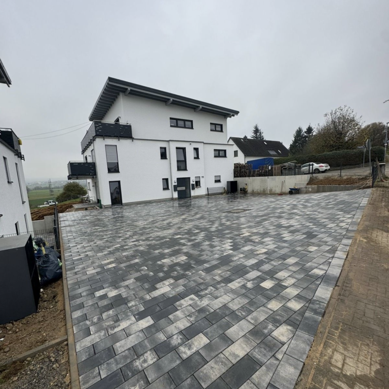 Moderne weiße Gebäude umgeben von einem gepflasterten Parkplatz in grauer Umgebung.
