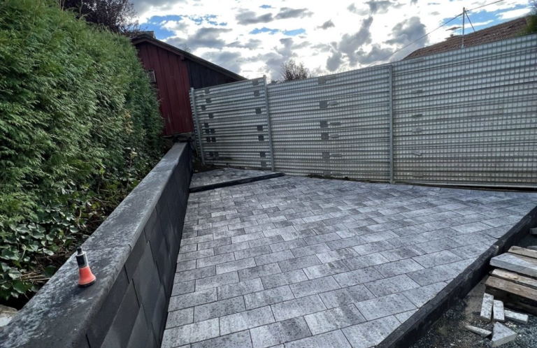 Gepflasterter Innenhof mit einer Mauer und Holzzaun im Hintergrund.