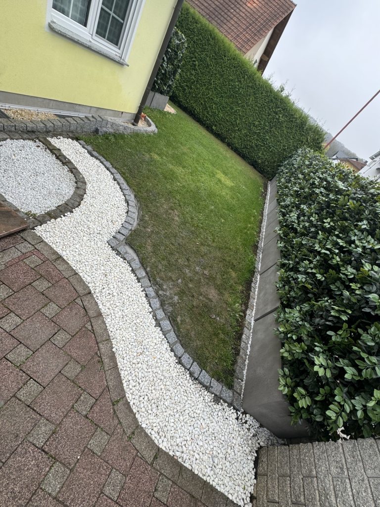 Gepflasterter Weg mit Kies und Rasenfläche neben einem gelben Haus.