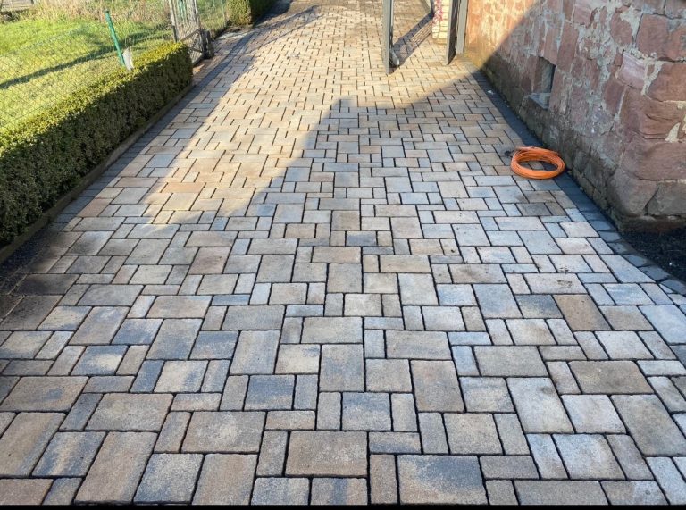 Pflasterweg mit geometrischen Steinen, auf einer Seite ein Rasen und ein Spielring.